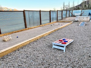 Un camp de petanca amb una banca de fusta, un joc de pilotes de petanca i una tanca metàl·lica.