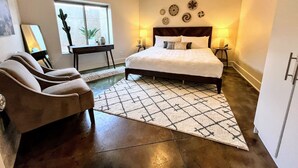 A bedroom with a bed, two bedside tables, a chair, a rug, and a window with plants. - MtnViews–Hot tub-Mini Golf–Bocce–Pool Table–3000sf (Moab)