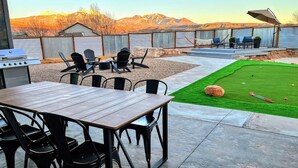 An outdoor patio with a table and chairs, a grill, and a small lawn with a rock and golf ball. - MtnViews–Hot tub-Mini Golf–Bocce–Pool Table–3000sf (Moab)