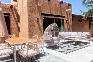 An outdoor seating area with a wooden table and chairs, a cushioned sofa, and a hanging chair. - MiniGolf–PoolTable–FirePit–BBQ–Arcade–Bocce Ball (Page)