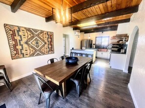 A dining area with a wooden table and chairs, a rug, and a kitchen in the background. - NEW! MiniGolf–PoolTable–FirePit–BBQ–Arcade–Bocce (Page)