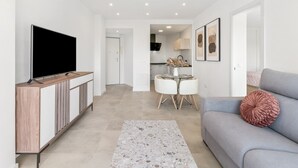 Een moderne woonkamer met een flatscreen televisie, een grijze bank en een eethoek met een kleine tafel en stoelen.