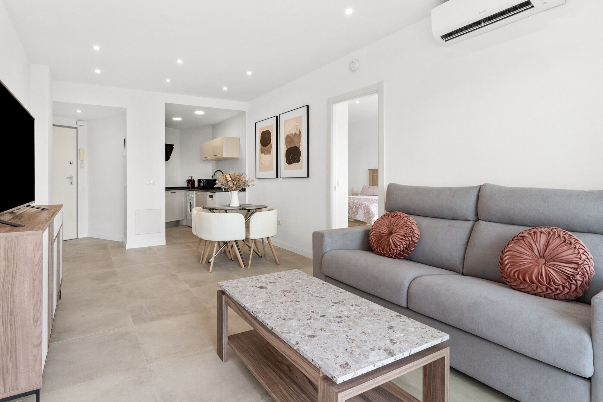 Un salon moderne avec un canapé gris, une table basse en bois et un coin repas comprenant une table et des chaises blanches.