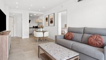 A modern living room with a grey sofa, a wooden coffee table, and a dining area with a white table and chairs.