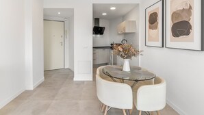 Een moderne keuken met witte kasten, een zwarte afzuigkap en een eetgedeelte met een glazen tafel en witte stoelen.