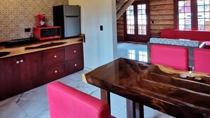 A rustic interior with a wooden ceiling, a kitchen area with a microwave, and a dining area with red chairs. - Hotel Bellotas Resort (Badiraguato)