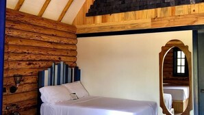 A bedroom with two beds, wooden beams, a sloped ceiling, and a large mirror. - Hotel Bellotas Resort (Badiraguato)