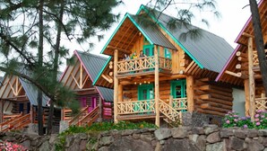 A wooden cabin with a balcony, surrounded by trees and a stone wall. - Hotel Bellotas Resort (Badiraguato)