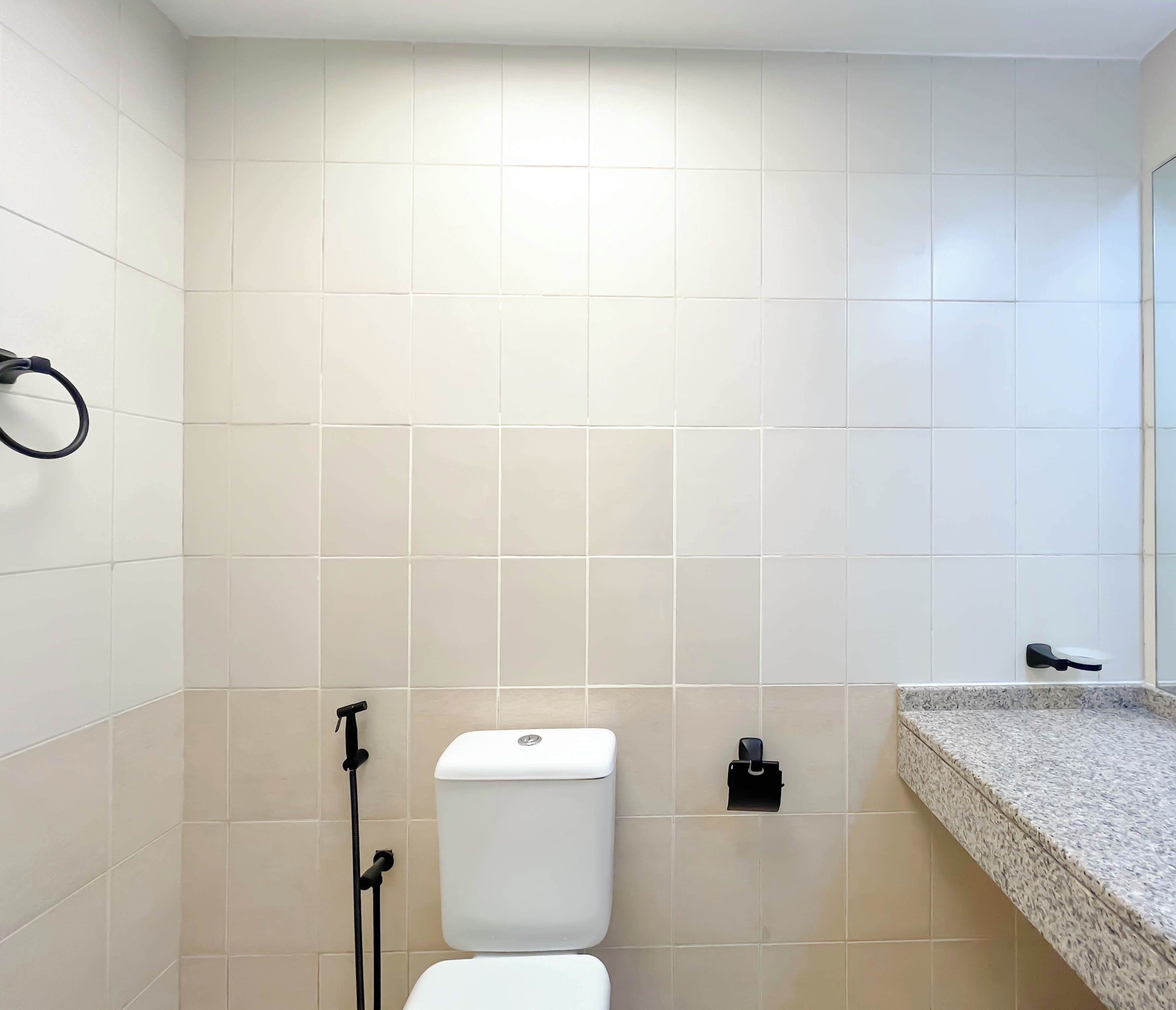 A bathroom with white tiles, a toilet, a bidet, a towel rack, and a granite countertop.