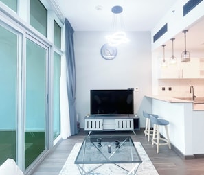 Een moderne woonkamer met een glazen salontafel, een flatscreen televisie en een eethoek met barstoelen.