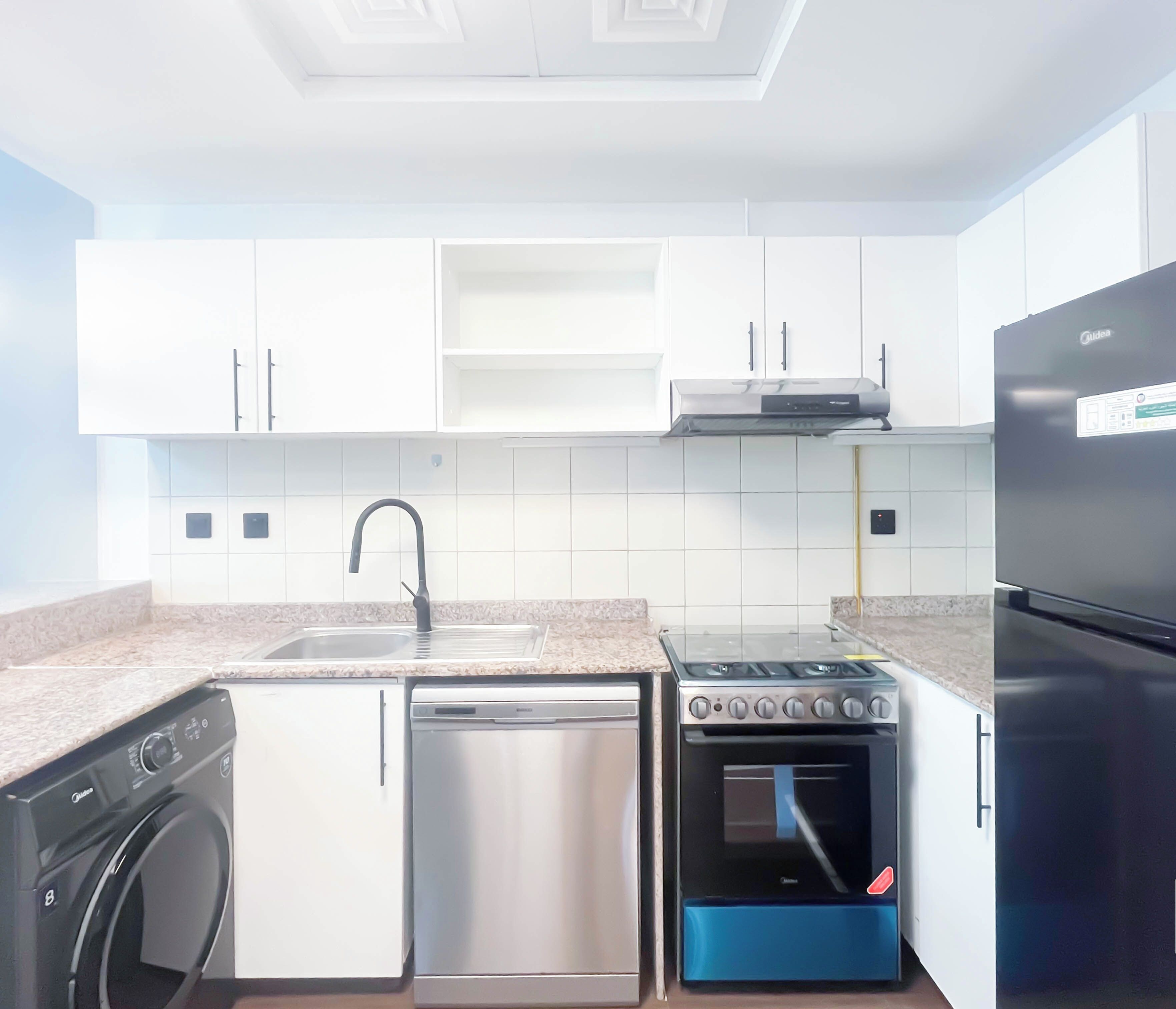 Eine moderne Küche mit weißen Schränken, einem Edelstahl-Geschirrspüler, einem eingebauten Backofen und einem schwarzen Kühlschrank.
