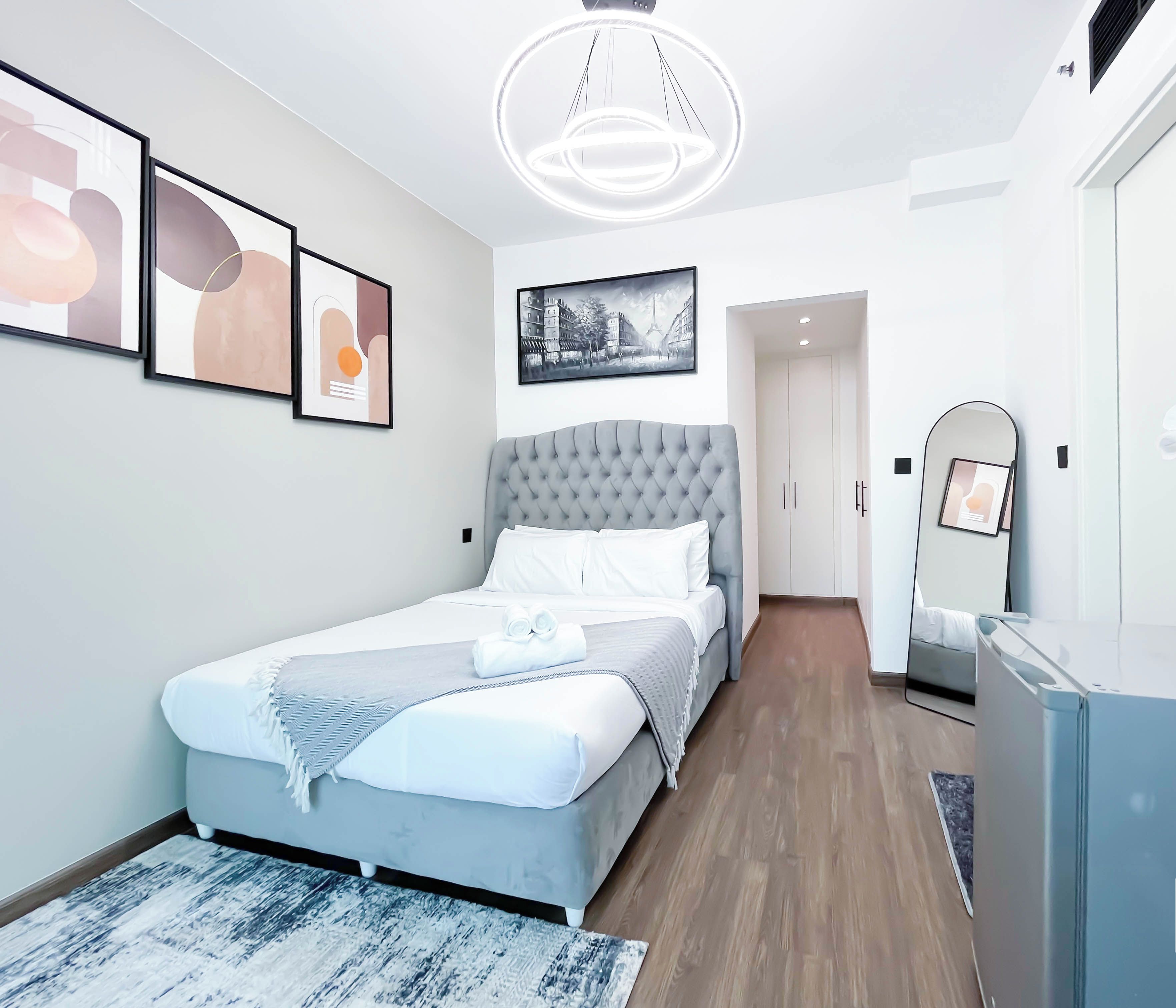 A modern hotel room with a large bed, a wardrobe, a mirror, and a ceiling light fixture.