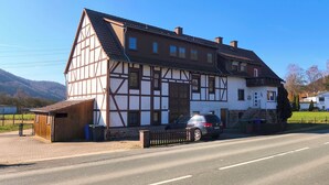 Une maison traditionnelle à colombages, avec une voiture garée devant, une route pavée et un ciel dégagé.