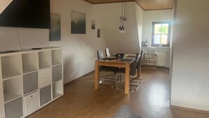 Un vaste espace de vie comprenant une table à manger en bois, des chaises, un canapé et un téléviseur fixé au mur.