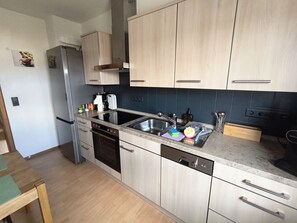 A modern kitchen with light wood cabinets, stainless steel appliances, and a built-in dishwasher. - Vacation apartment with pony farm 🐴🐶🐓 (Edertal)