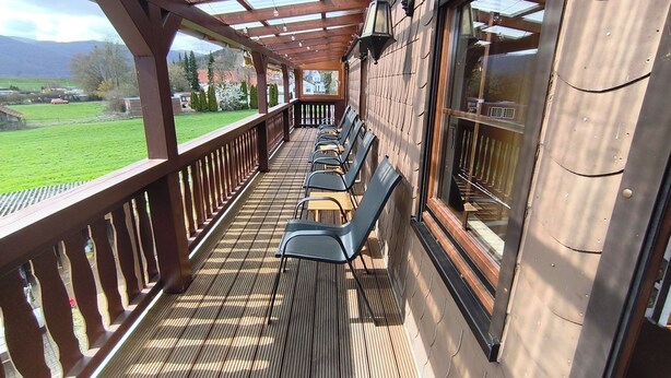 Un espace extérieur aménagé, abrité et doté d’un plancher en bois, de rampes en métal et offrant une vue sur un paysage verdoyant.