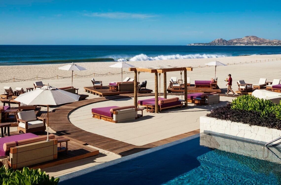 A resort pool area with lounge chairs and umbrellas, a wooden deck, and a view of the ocean.