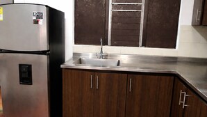 A kitchen with a stainless steel refrigerator, a sink, and wooden cabinets. - Room AREAS by QuBeLab (Bello)