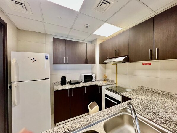 A compact kitchen with dark wooden cabinets, a white refrigerator, a microwave, a coffee maker, and a gas stove.