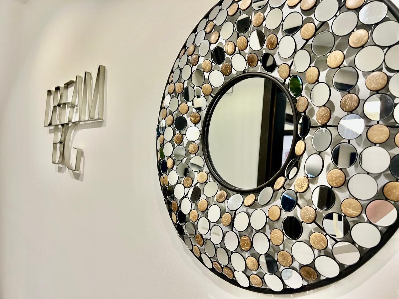 A wall with a circular mirror surrounded by a mosaic of variously shaped and colored mirrors.