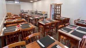 Un área de comedor con varias mesas y sillas de madera, dispuestas en filas.