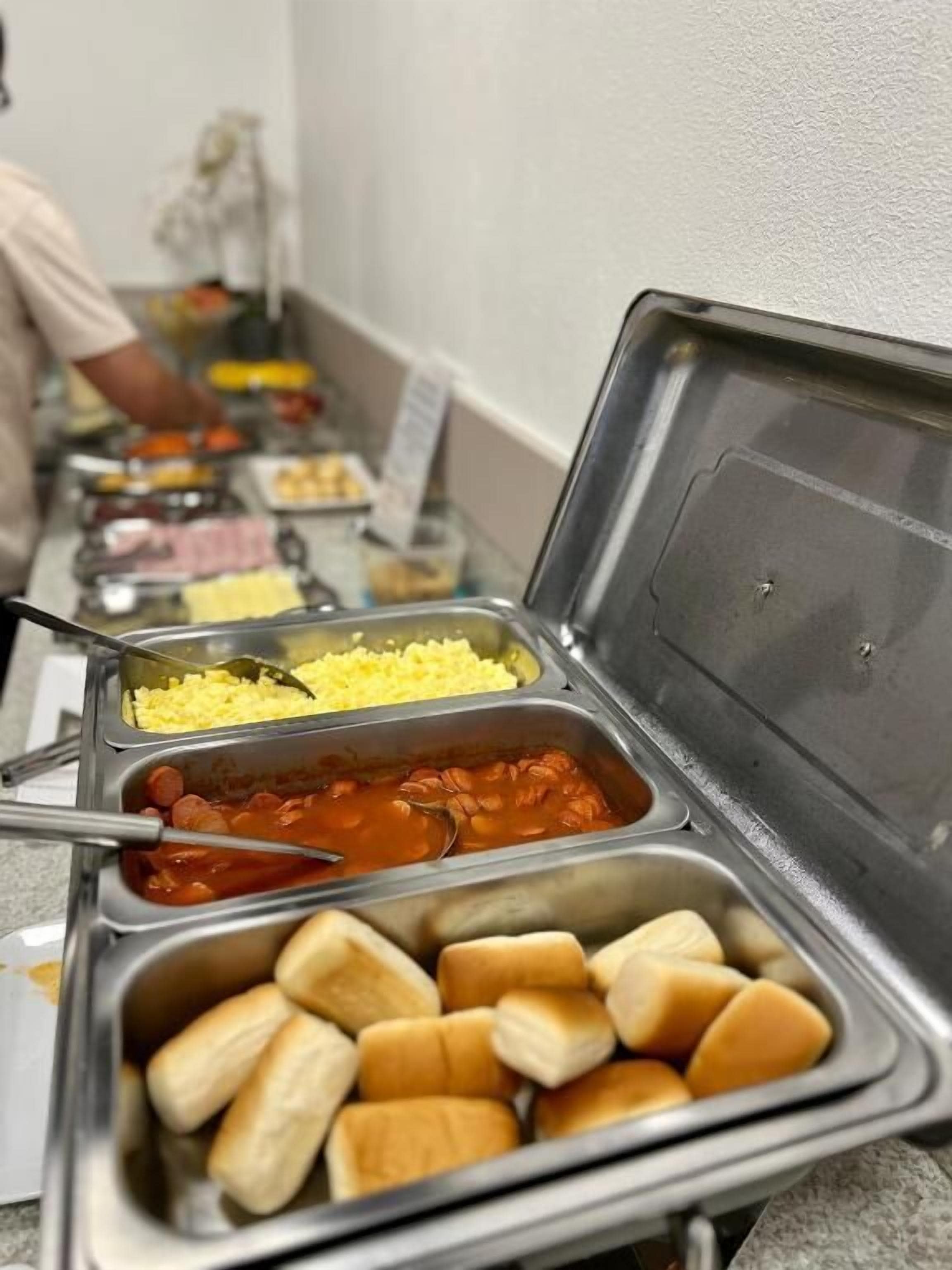 Un buffet proposant divers plats, notamment des œufs brouillés, des haricots et des petits pains.