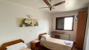 Una habitación con dos camas, ventilador de techo, ventana y radiador.