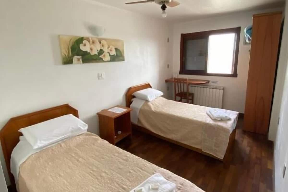 A room with two beds, a ceiling fan, a window, and a radiator.