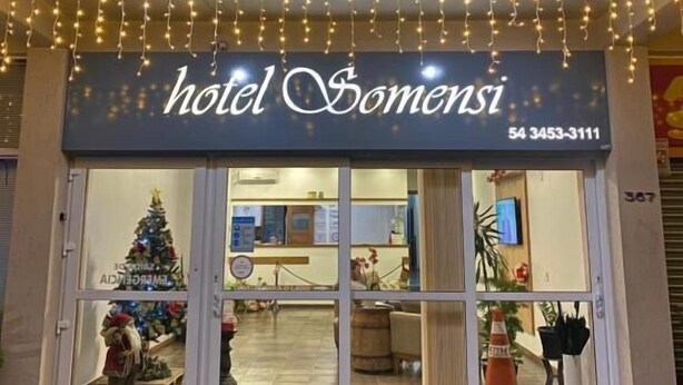 Entrada de un hotel con un letrero que dice "hotel SOMENSI" y un número de teléfono. Se ve una decoración de árbol de Navidad afuera de la entrada.