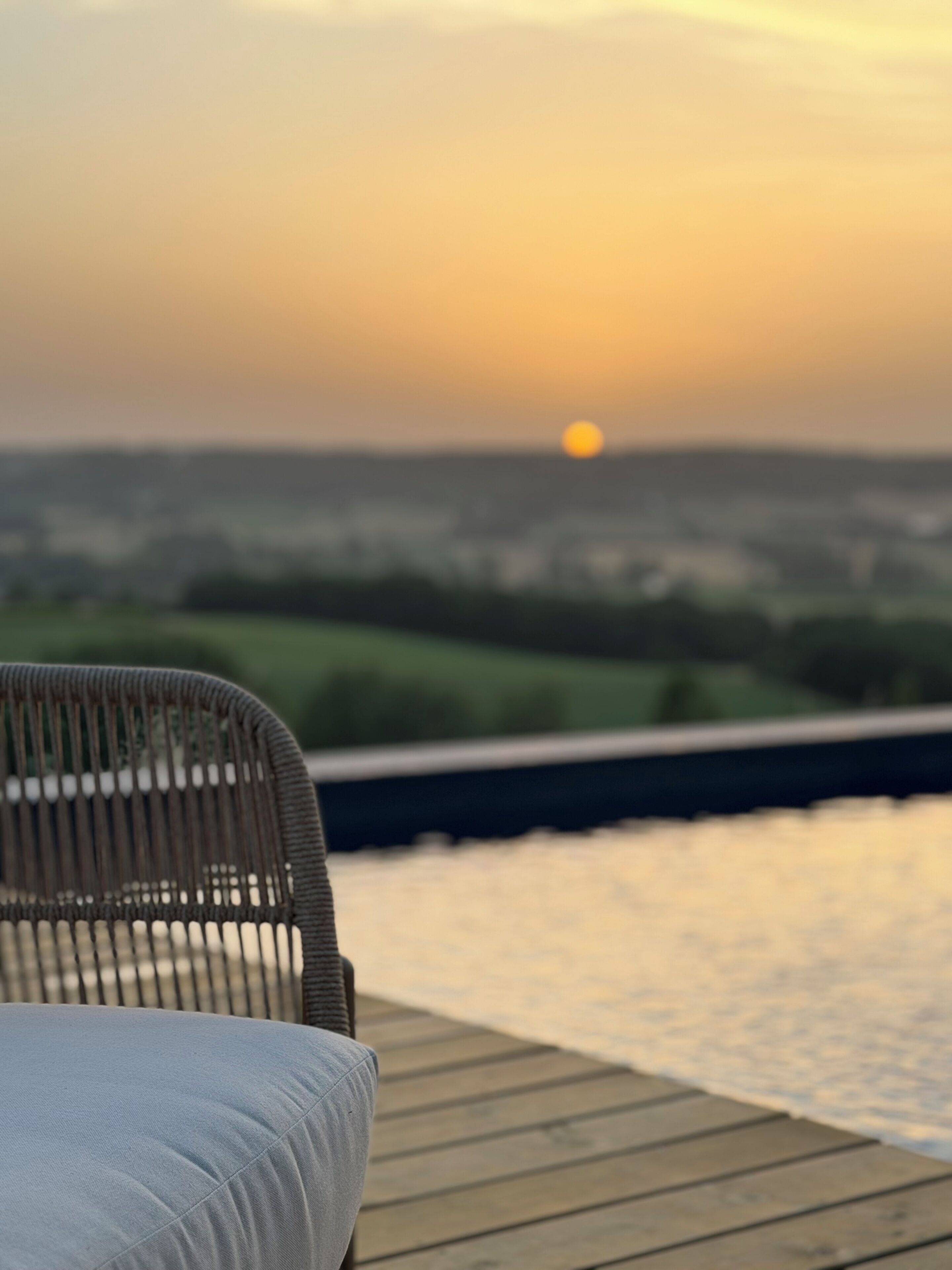 Une chaise sur une terrasse en bois donnant sur une étendue d’eau, avec un coucher de soleil en arrière-plan.
