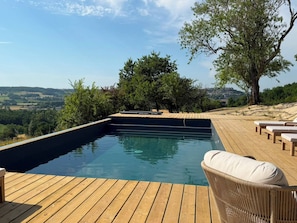Eine Holzterrasse mit Swimmingpool, Liegestühlen und Blick auf die Landschaft.