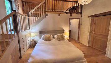 Une chambre à coucher avec un grand lit, un plancher en bois, un escalier et un lustre.