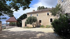 Un bâtiment en pierre avec un toit en tuiles, un espace extérieur abrité avec des sièges et une allée gravillonnée.