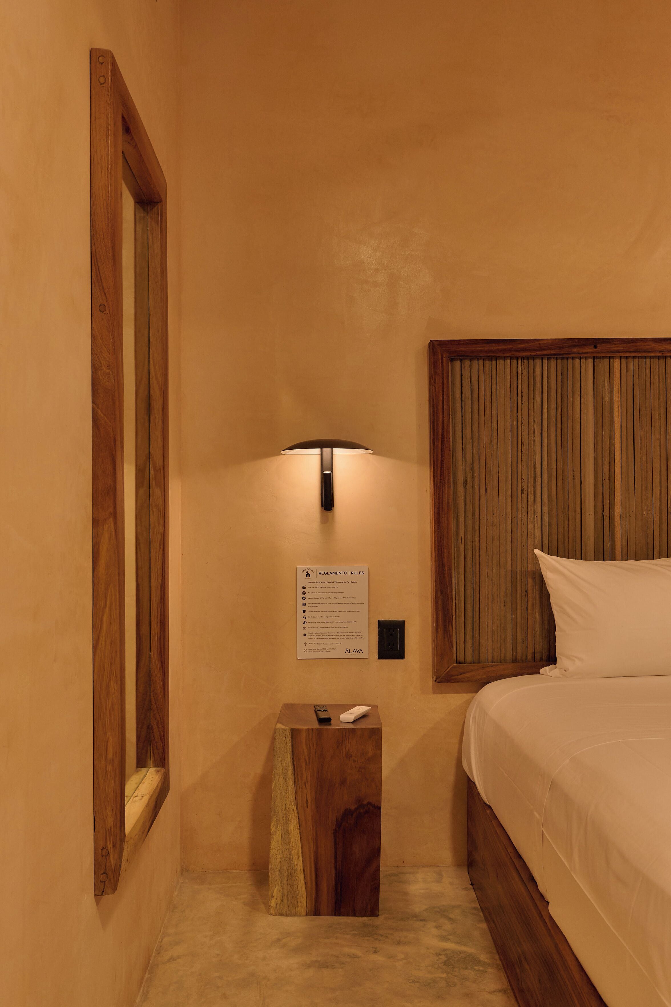 A hotel room with a wooden headboard, a bedside table with a remote control, and a wall-mounted light fixture.