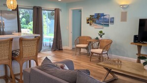 Un salon moderne avec un canapé, des fauteuils en osier, une table à manger en bois et un meuble pour la télévision.