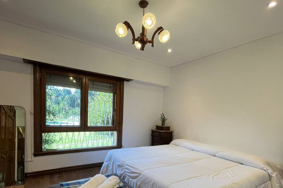 Quarto com uma cama grande, um banquinho com toalhas, uma pequena mesa com uma planta e uma janela com vista para o verde.
