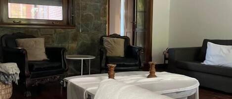 A living room with a round table, two sofas, a stone wall, and a window with blinds.