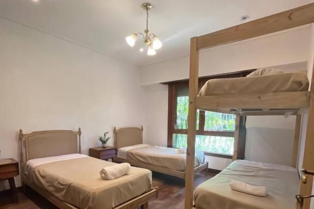Quarto com três beliches de madeira, assoalho de madeira, luminária no teto e janela com vista para área verde.