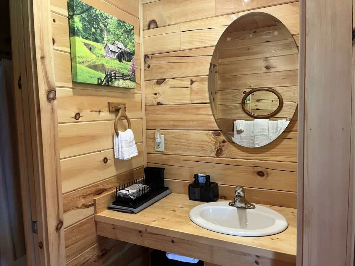 A wooden cabin-style bathroom with a wooden vanity, a sink, a mirror, and a towel rack.