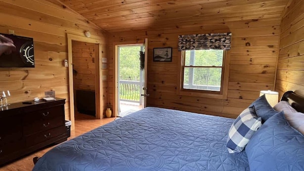 Un dormitorio de cabaña de madera con cama, cómoda y ventana con vistas.