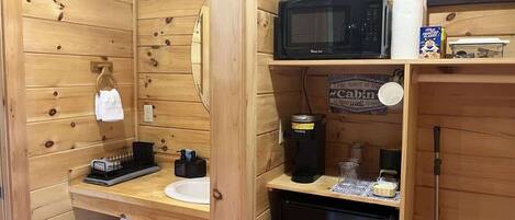 Una cabaña compacta con interior de madera, microondas, cafetera, lavamanos y un refrigerador pequeño.