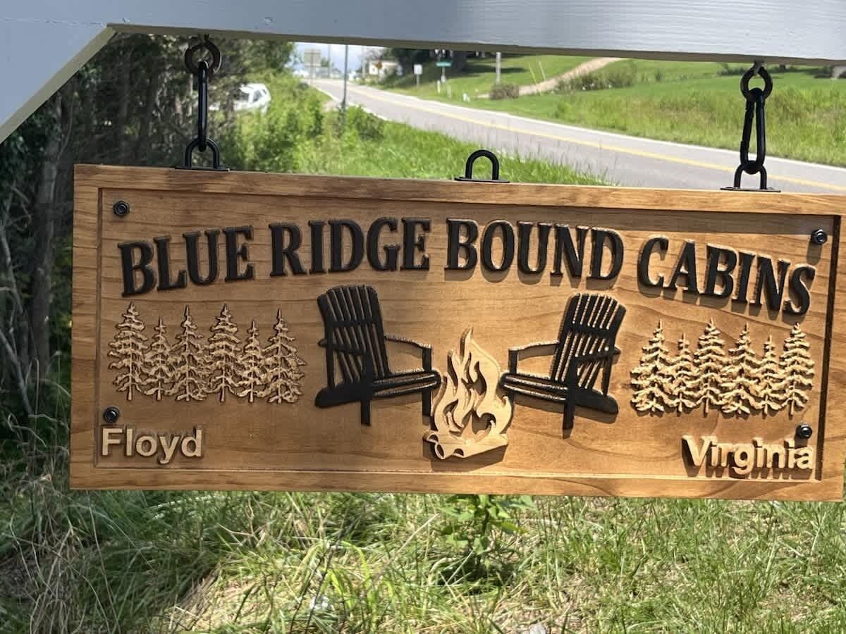 Une enseigne en bois pour le complexe de chalets « Blue Ridge Bound Cabins » situé à Floyd, en Virginie, représentant un chalet, des arbres et un feu de camp.