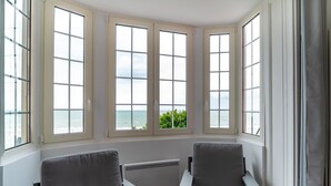 A room with three large windows, a radiator, and two grey chairs.