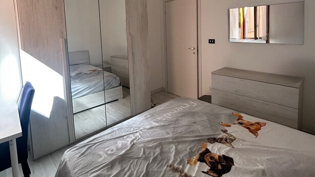A bedroom with a bed, a mirror, a dresser, and a wardrobe.