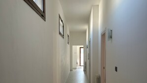 A hallway with light-colored walls, a wooden floor, and a door at the end.