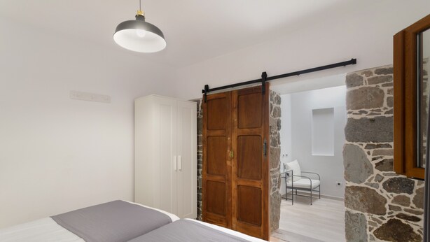 A bedroom with a bed, a wardrobe, a sliding door, and a stone wall.