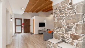 A modern living room with a stone accent wall, a flat-screen TV, a grey sofa, and a wooden ceiling.