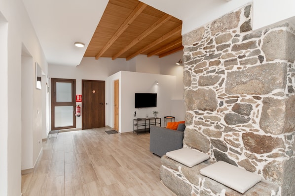 Ein modernes Wohnzimmer mit einer Wand aus Stein, einem Flachbildfernseher, einem grauen Sofa und einer Holzbalkendecke.