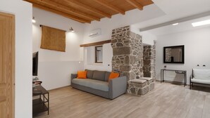 A modern living room with a stone wall, a grey sofa with orange cushions, a wooden ceiling, and a television.
