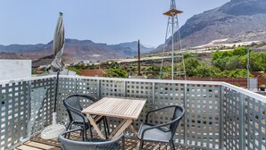 A balcony with a table and chairs, a view of mountains, and a power line tower.